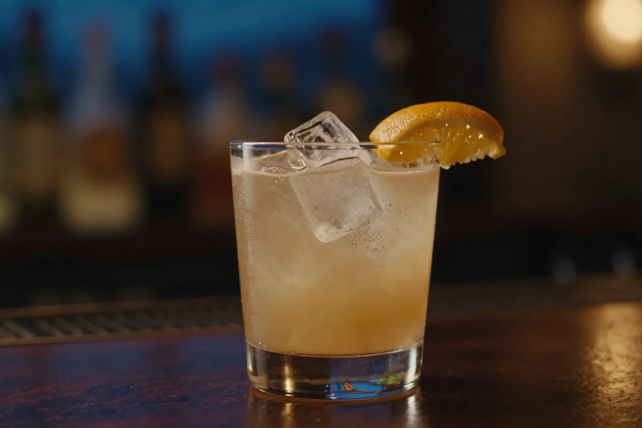 Cocktail signature servi sur bar, glaçon taillé, twist d'agrume